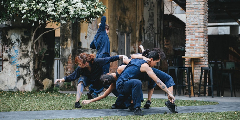 Group of dancers in blue costumes perform outdoors by an old building.